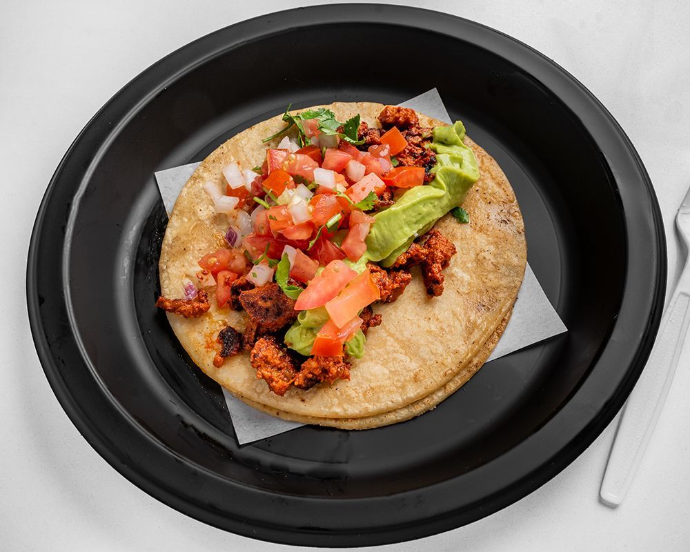 Taco on a black plate with meat, salsa, and guacamole.
