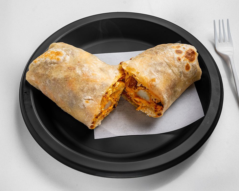 Burrito cut in half on a black plate with a white paper liner and a fork.