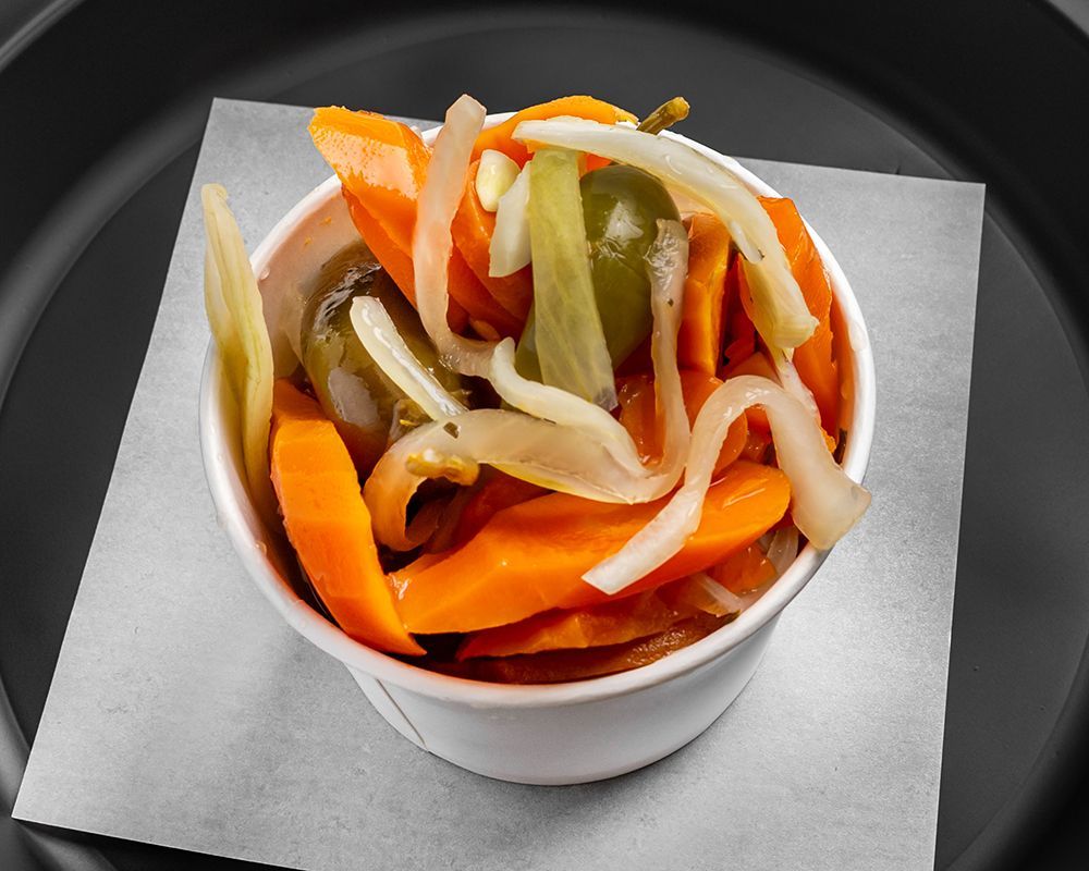 Pickled carrots, onions, and jalapeños in a white cup on a black plate.