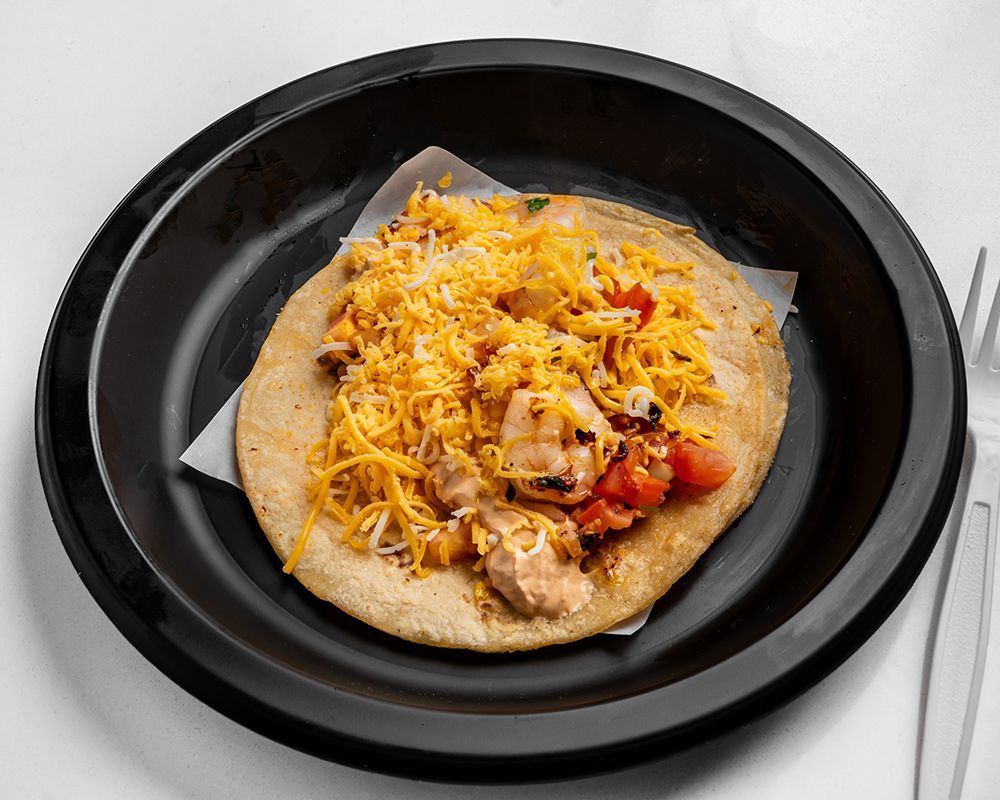 Flatbread topped with shredded cheese, chicken, and tomatoes in a black bowl.