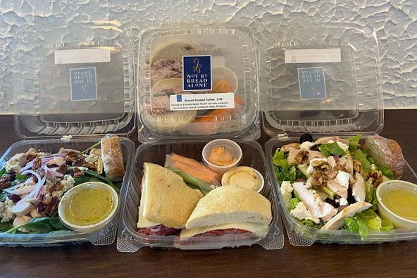 Three plastic containers of food are sitting on a wooden table.