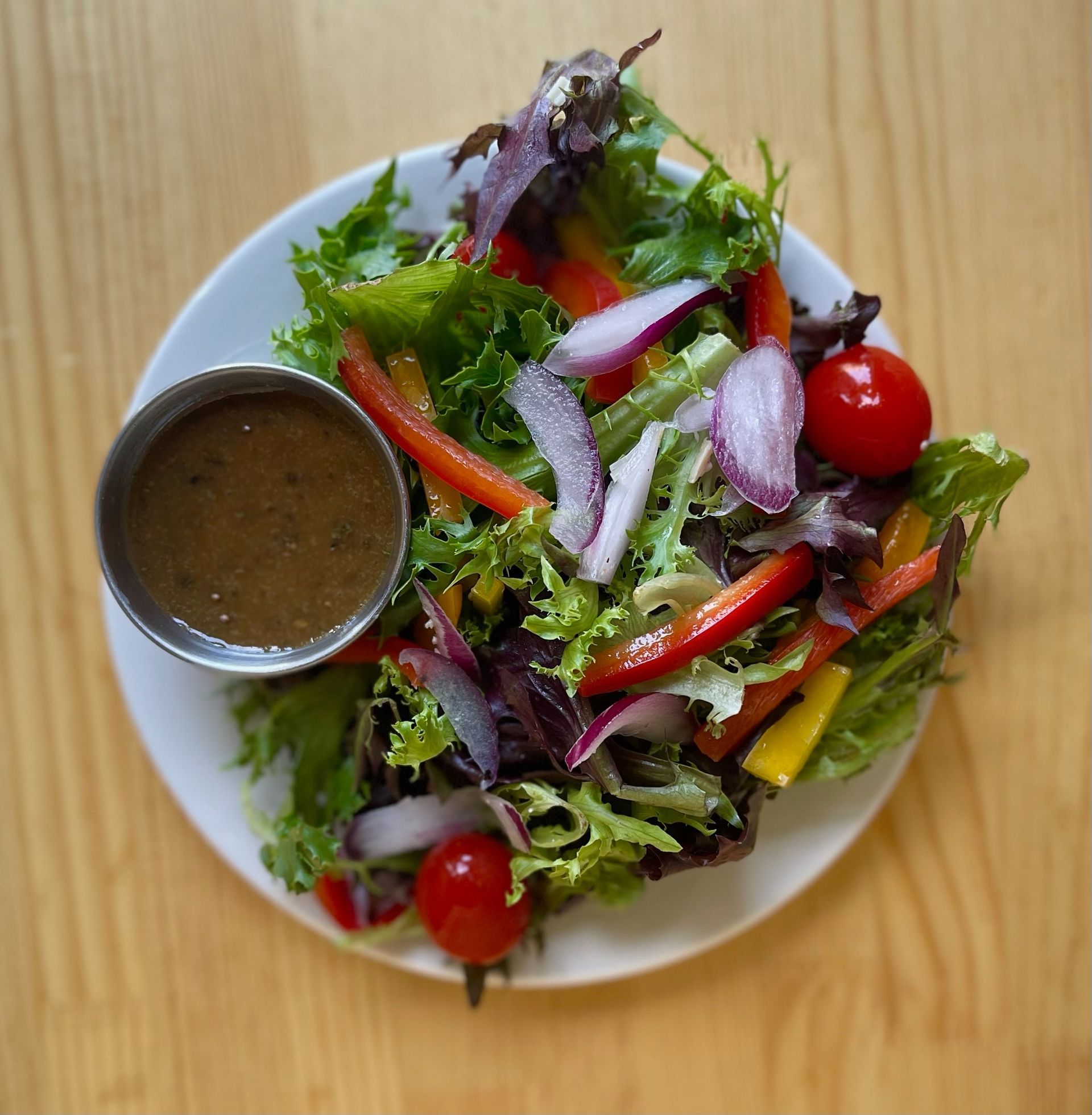 A white plate topped with a salad and a small bowl of dressing