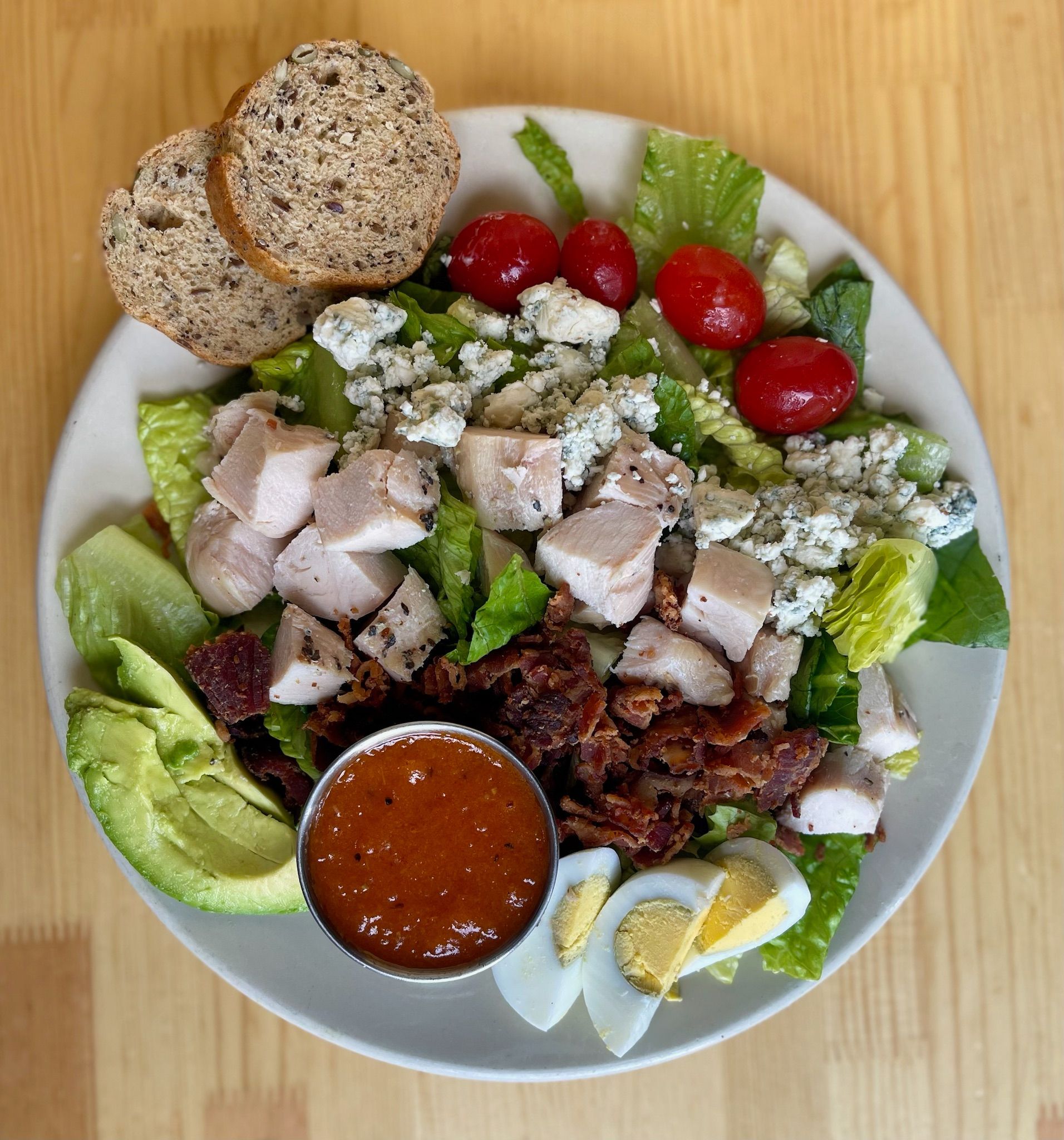 A salad with chicken, bacon, eggs, lettuce and avocado on a plate on a wooden table.