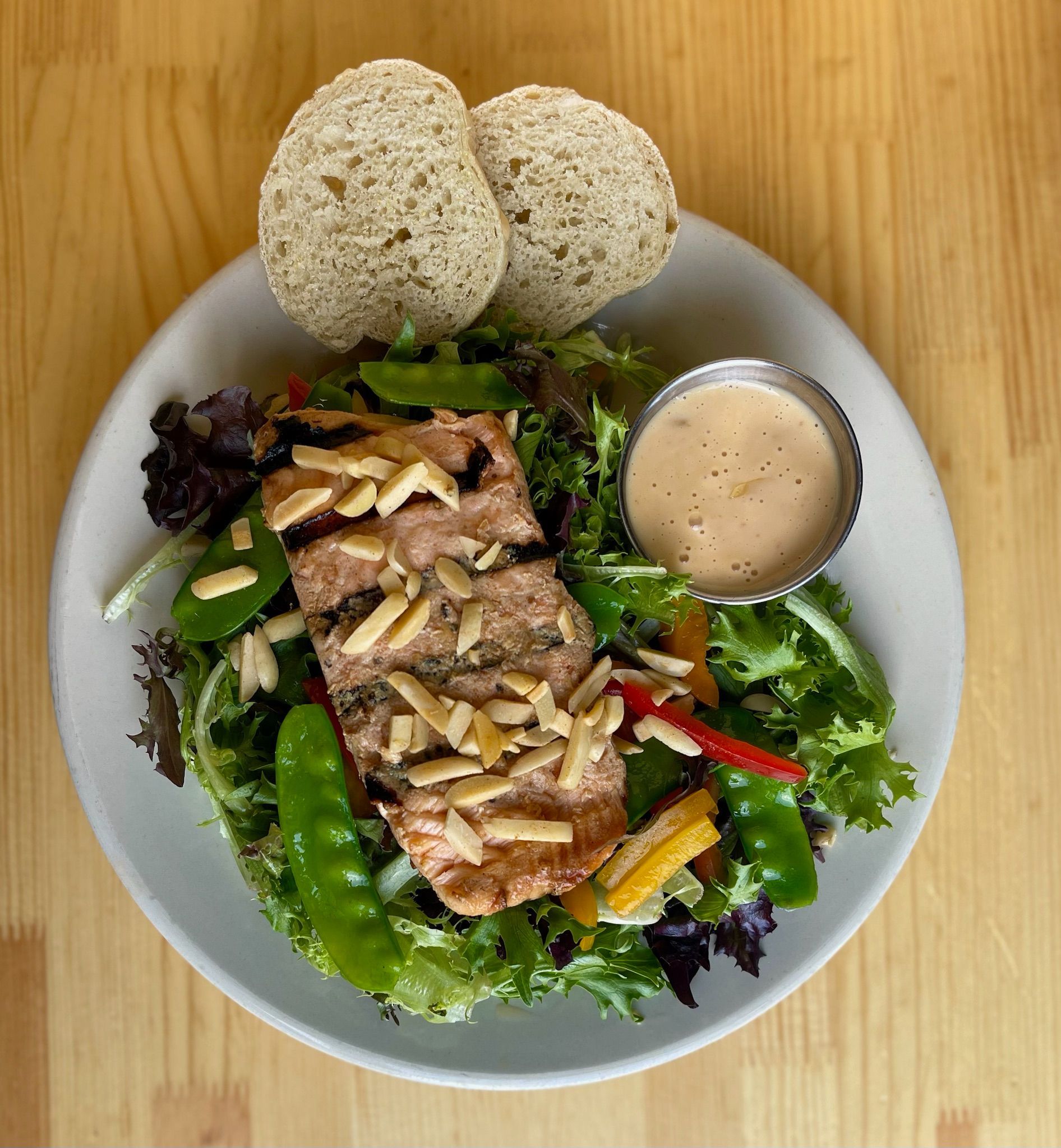 A white plate topped with a salad and bread on a wooden table.