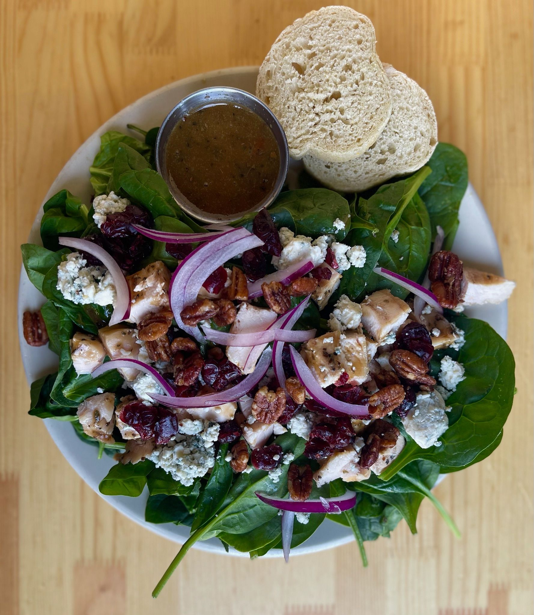 A salad with spinach, chicken, pecans, onions and a slice of bread on a plate.