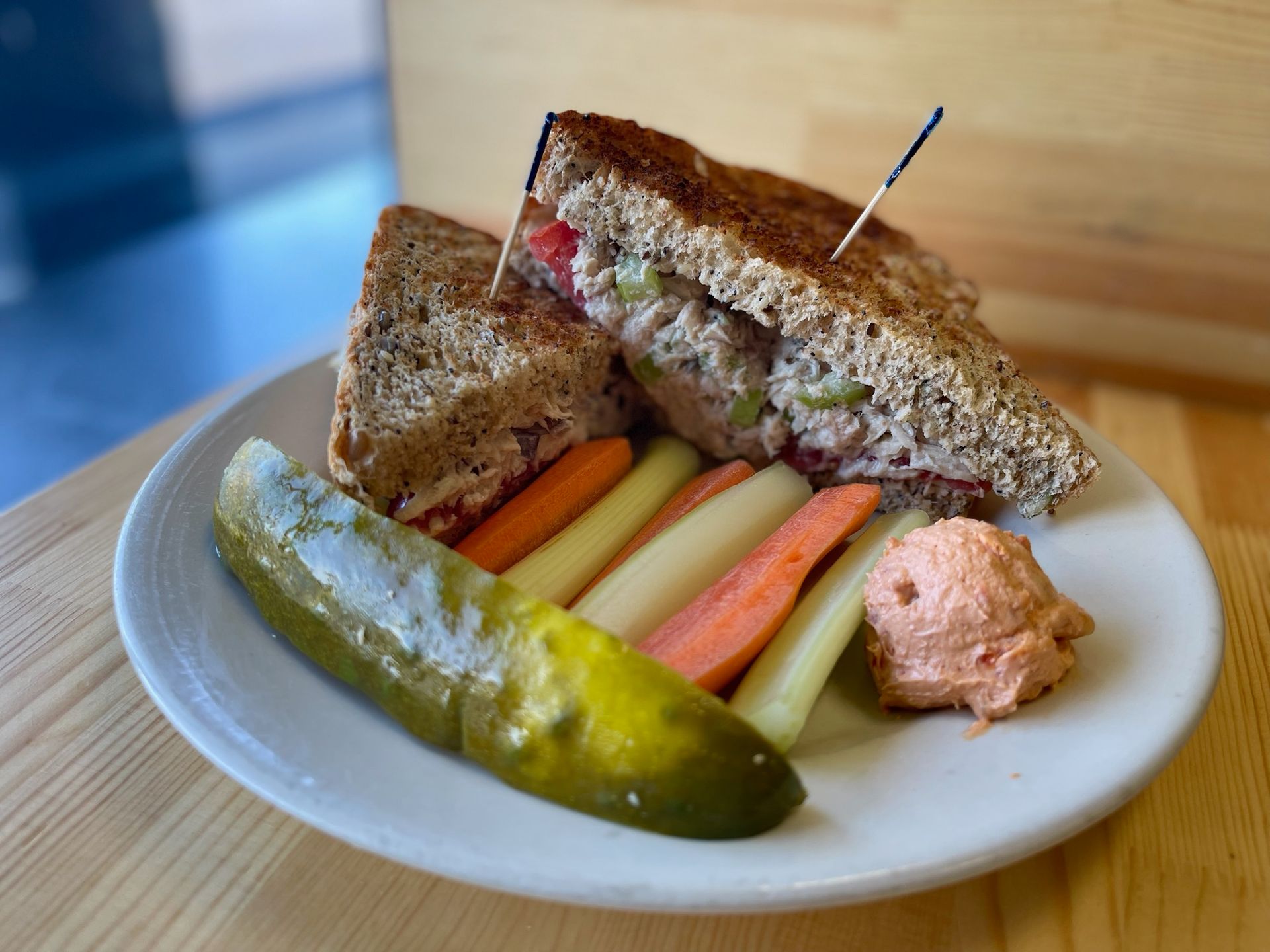 A white plate topped with a sandwich, pickles, carrots and hummus.
