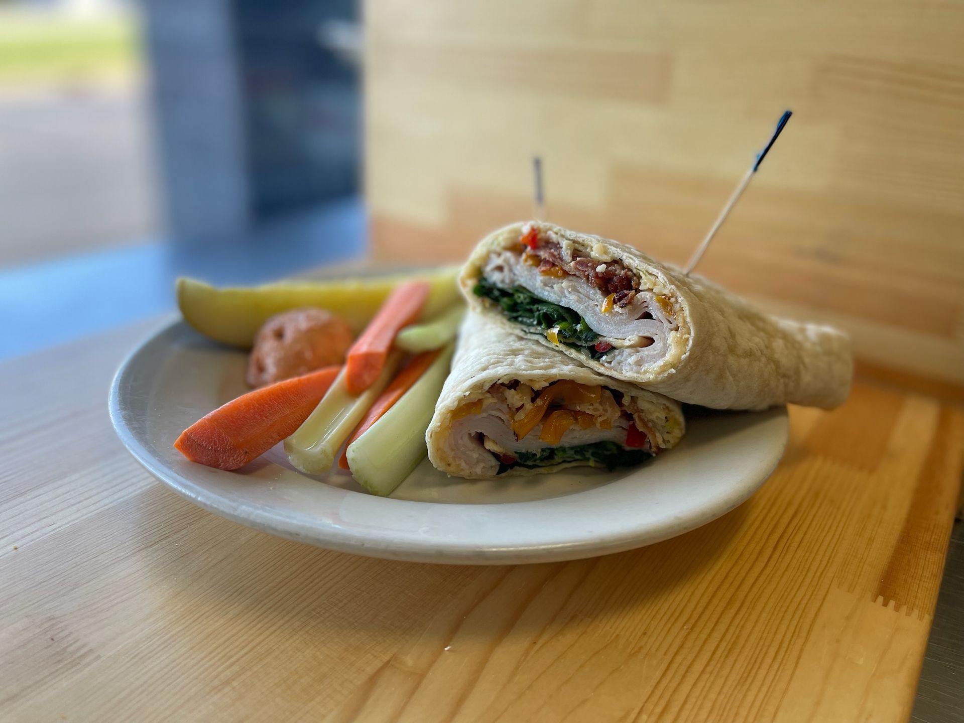 A wrap sandwich with vegetables on a plate on a wooden table.
