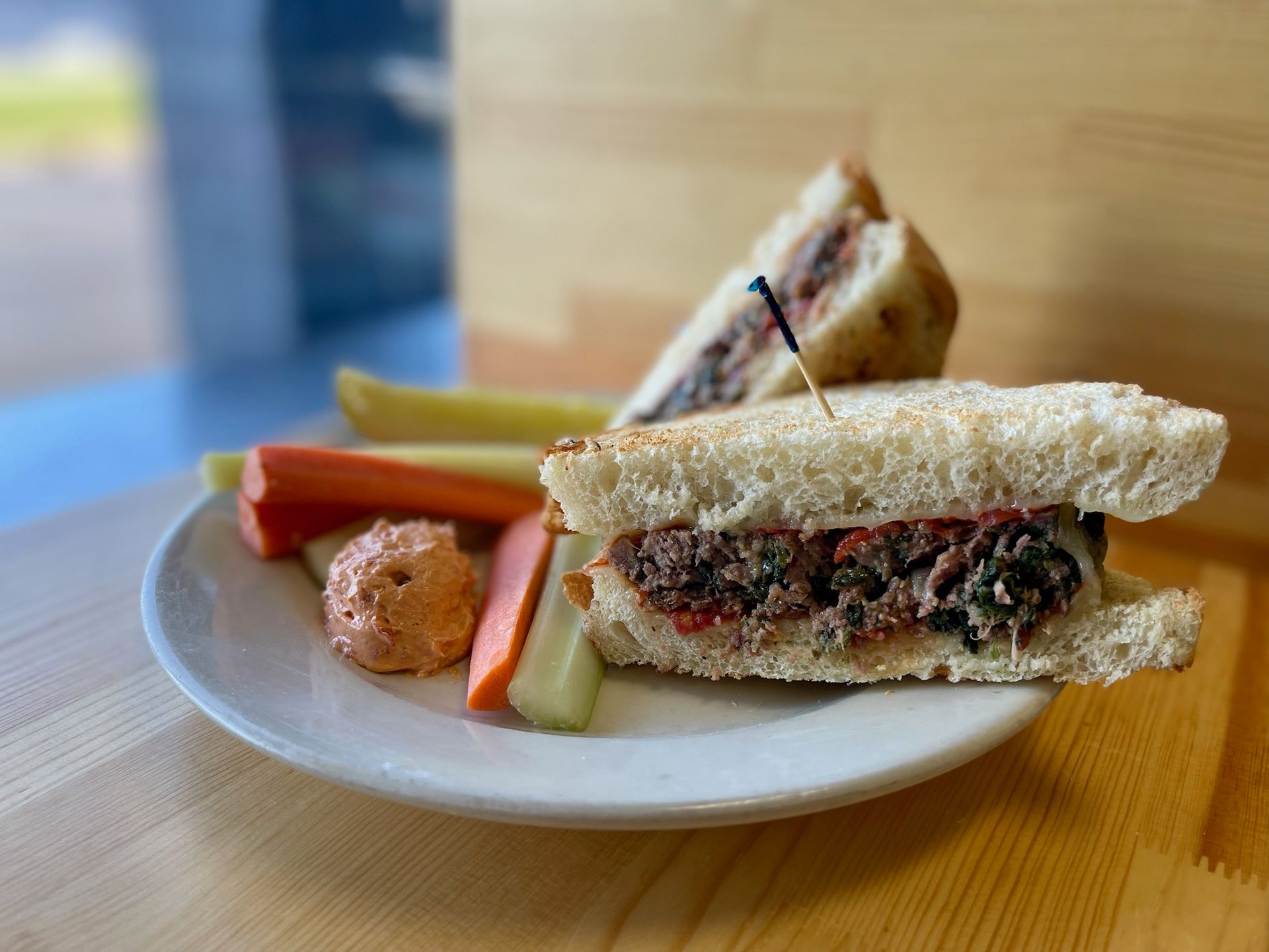 A sandwich and vegetables on a plate on a wooden table.