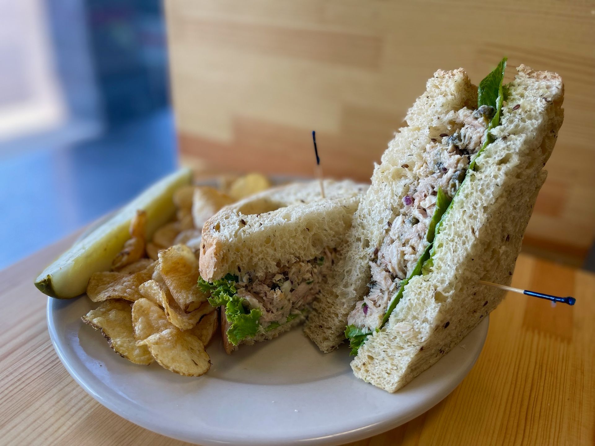 A sandwich on a plate with chips and a pickle.