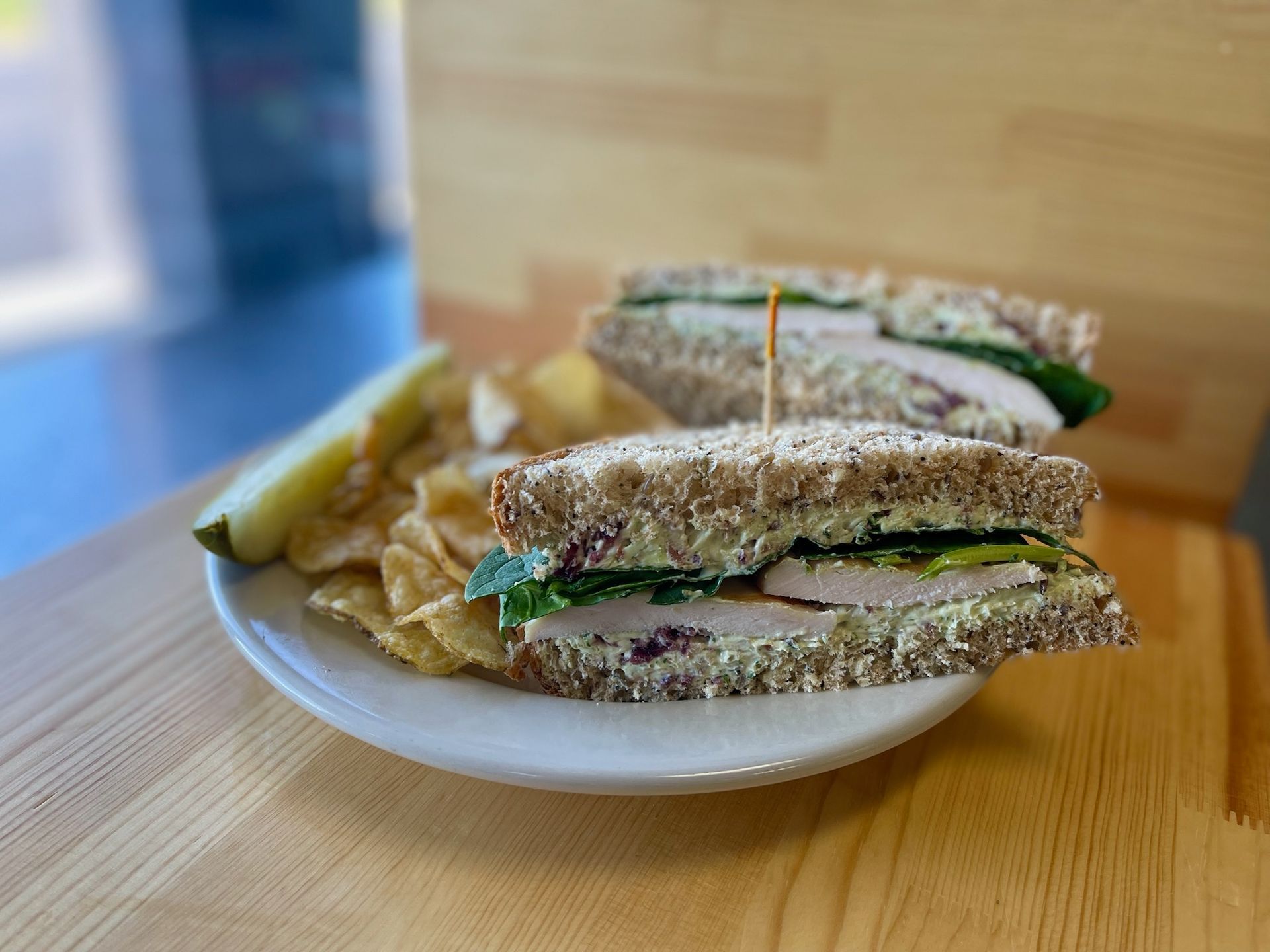 A sandwich and chips are on a white plate on a wooden table.