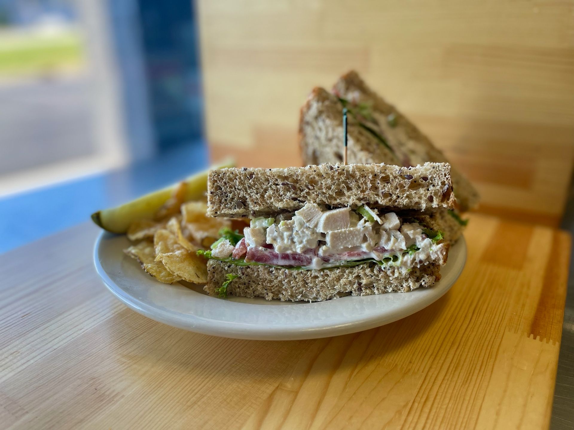 A chicken salad sandwich is on a white plate on a wooden table.
