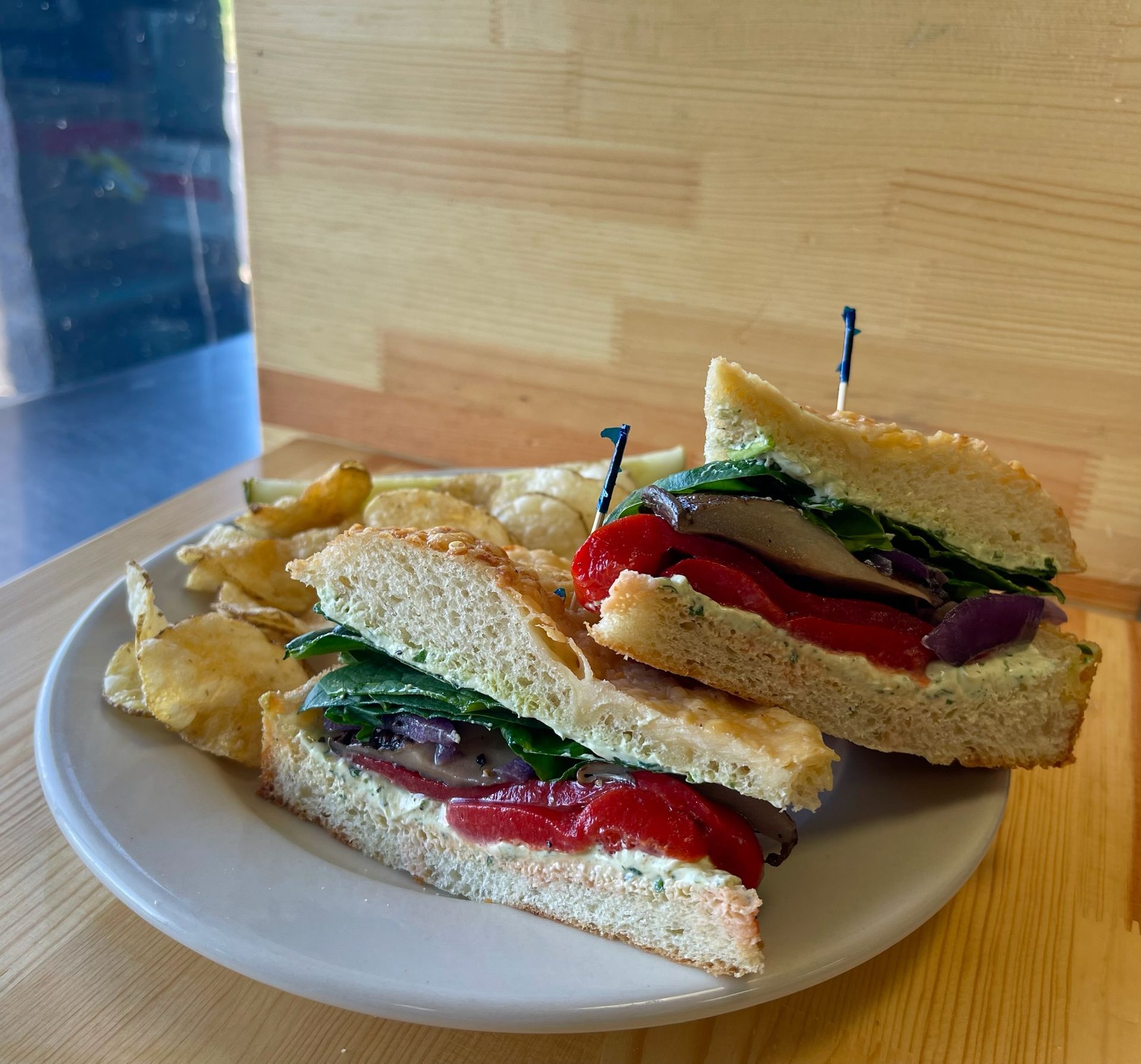 A white plate topped with sandwiches and chips on a wooden table.