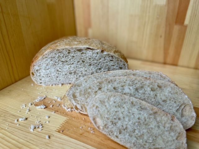 A loaf of bread is sitting on a wooden table next to two slices of bread.