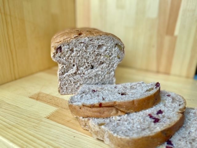 A loaf of bread is sitting on a wooden table next to slices of bread.