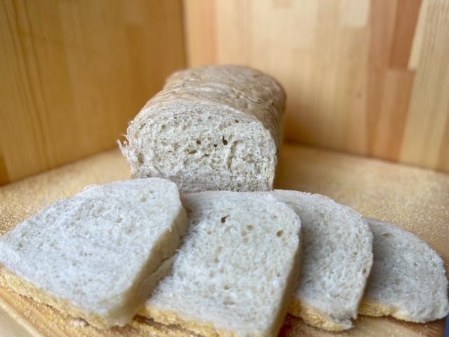 A loaf of bread is sitting on a wooden table next to slices of bread.