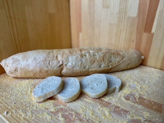 A loaf of bread is sitting on a wooden table next to slices of bread.