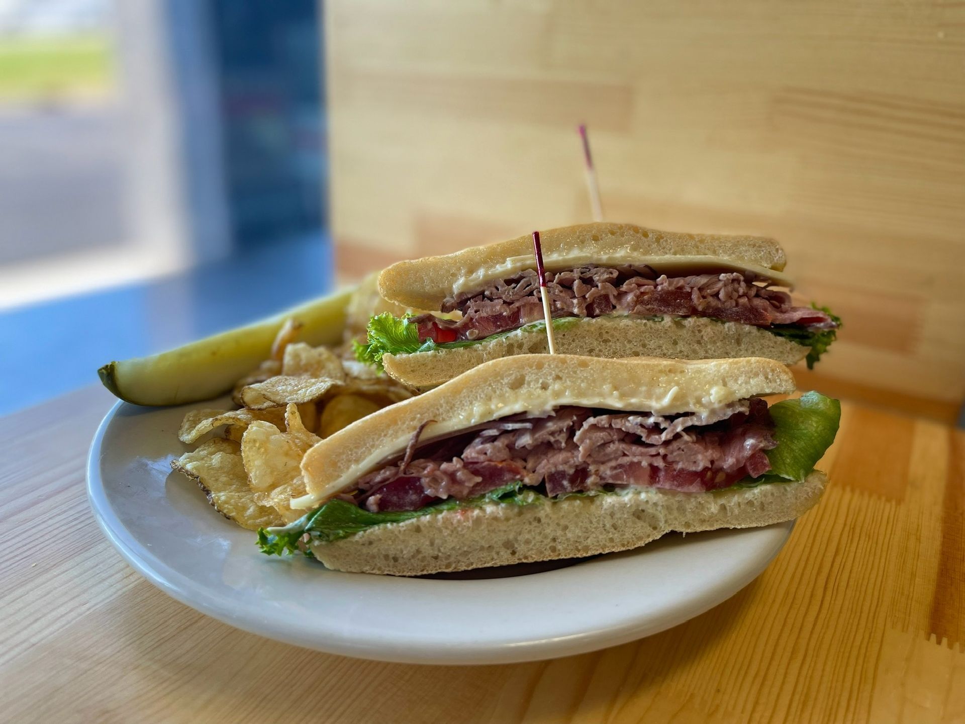 A sandwich with a pickle and chips on a plate on a table.