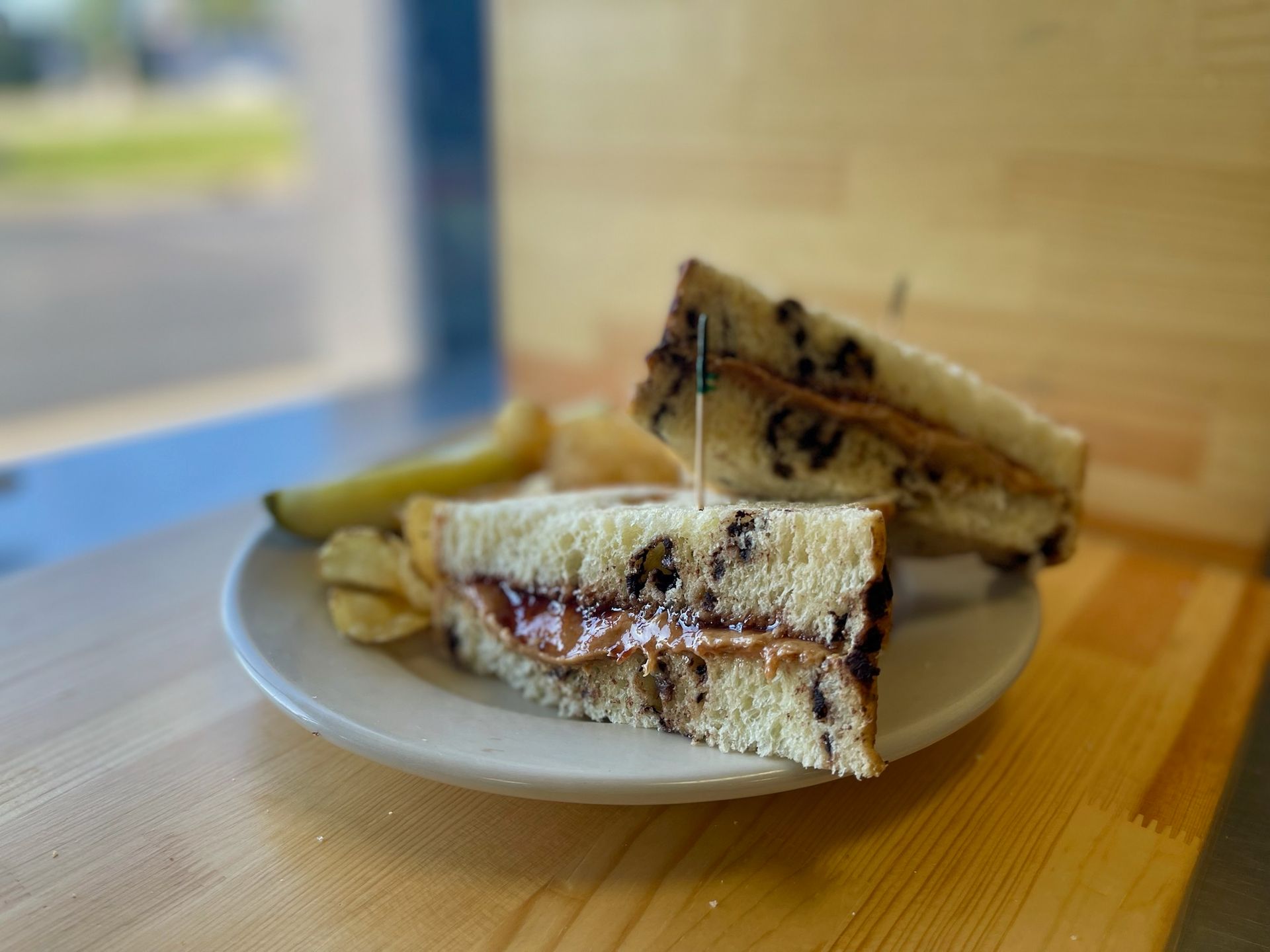 A peanut butter and jelly sandwich on a plate with chips and a pickle.