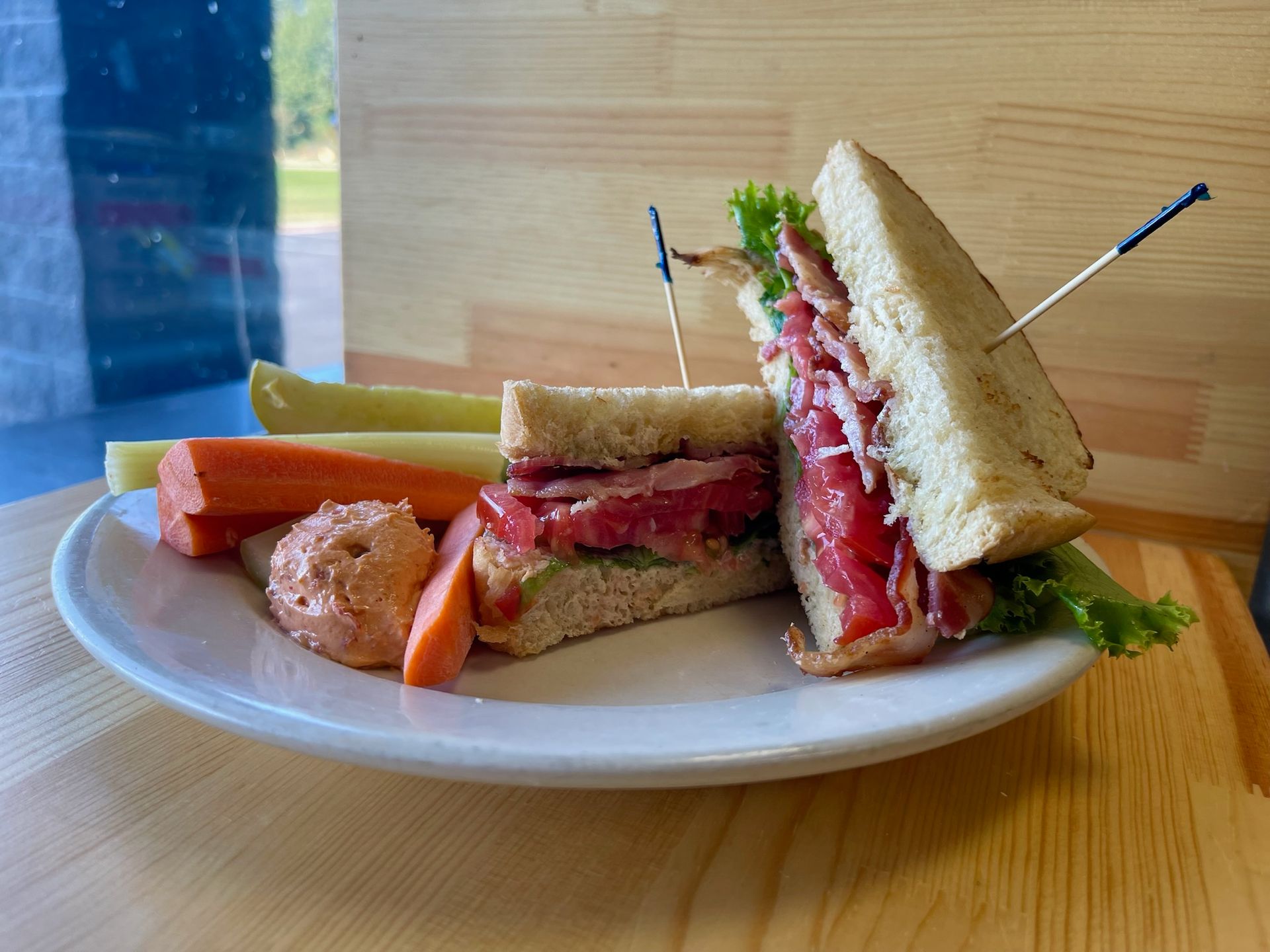 A sandwich and vegetables on a white plate on a wooden table.