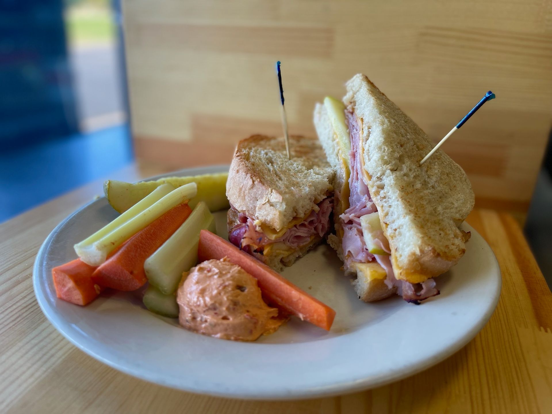 A sandwich and vegetables on a white plate on a wooden table.