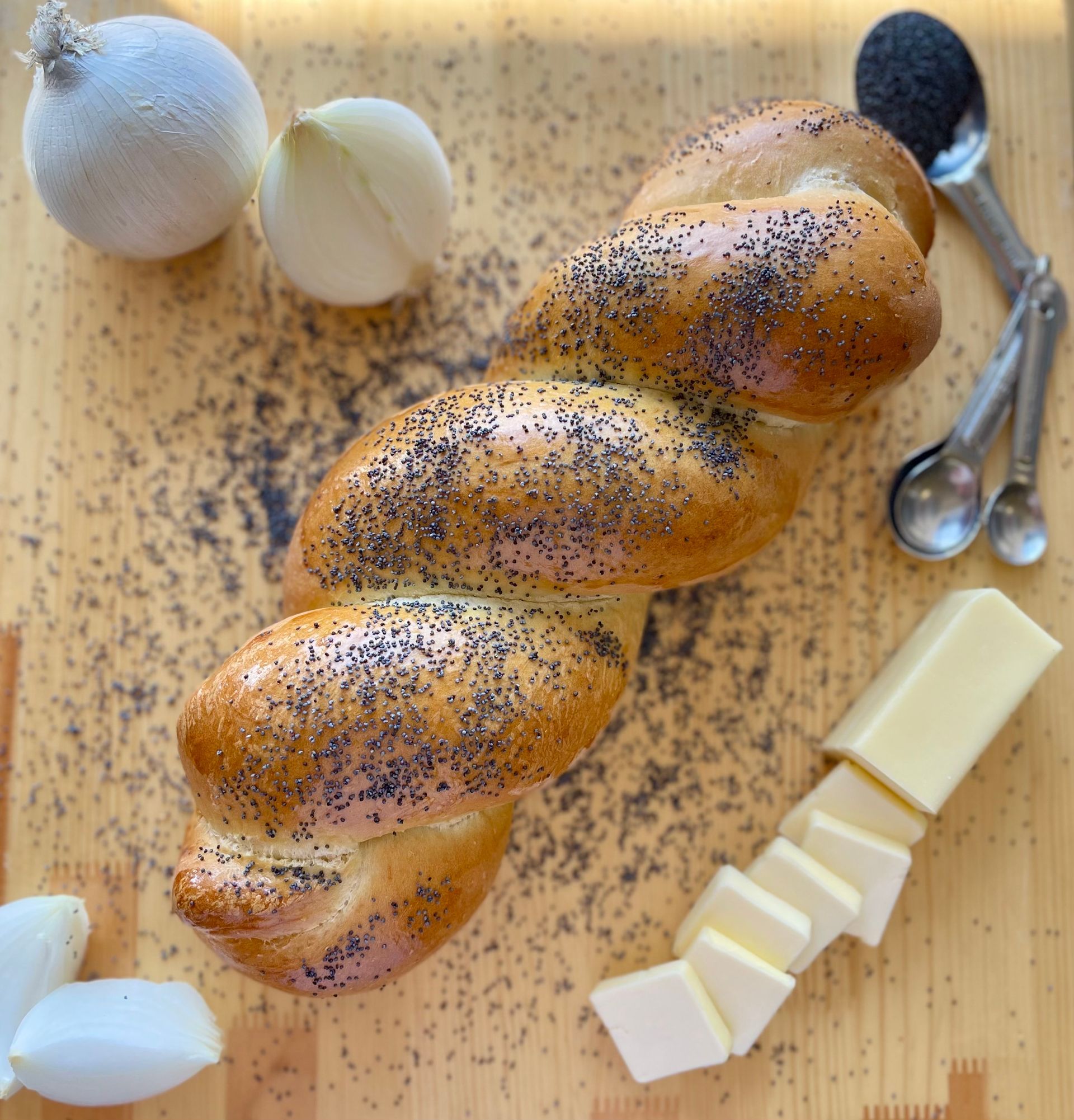 A loaf of bread is sitting on a wooden cutting board next to butter and onions.