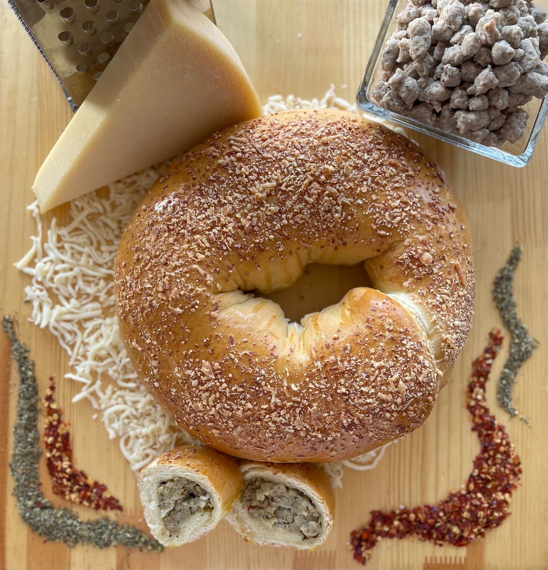 A bagel is sitting on a wooden cutting board surrounded by cheese and spices.