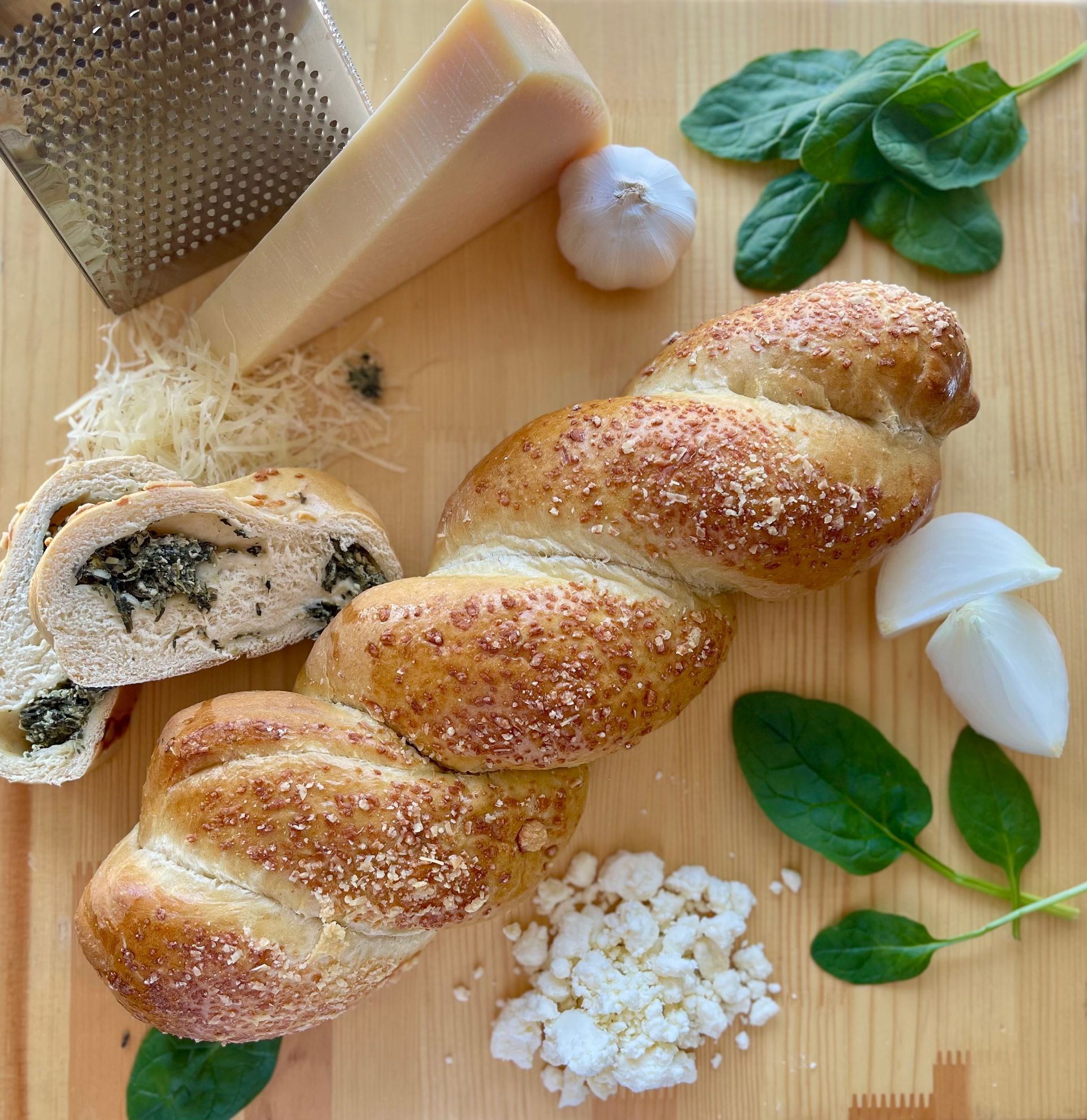 A loaf of bread is sitting on a wooden cutting board surrounded by vegetables and cheese.