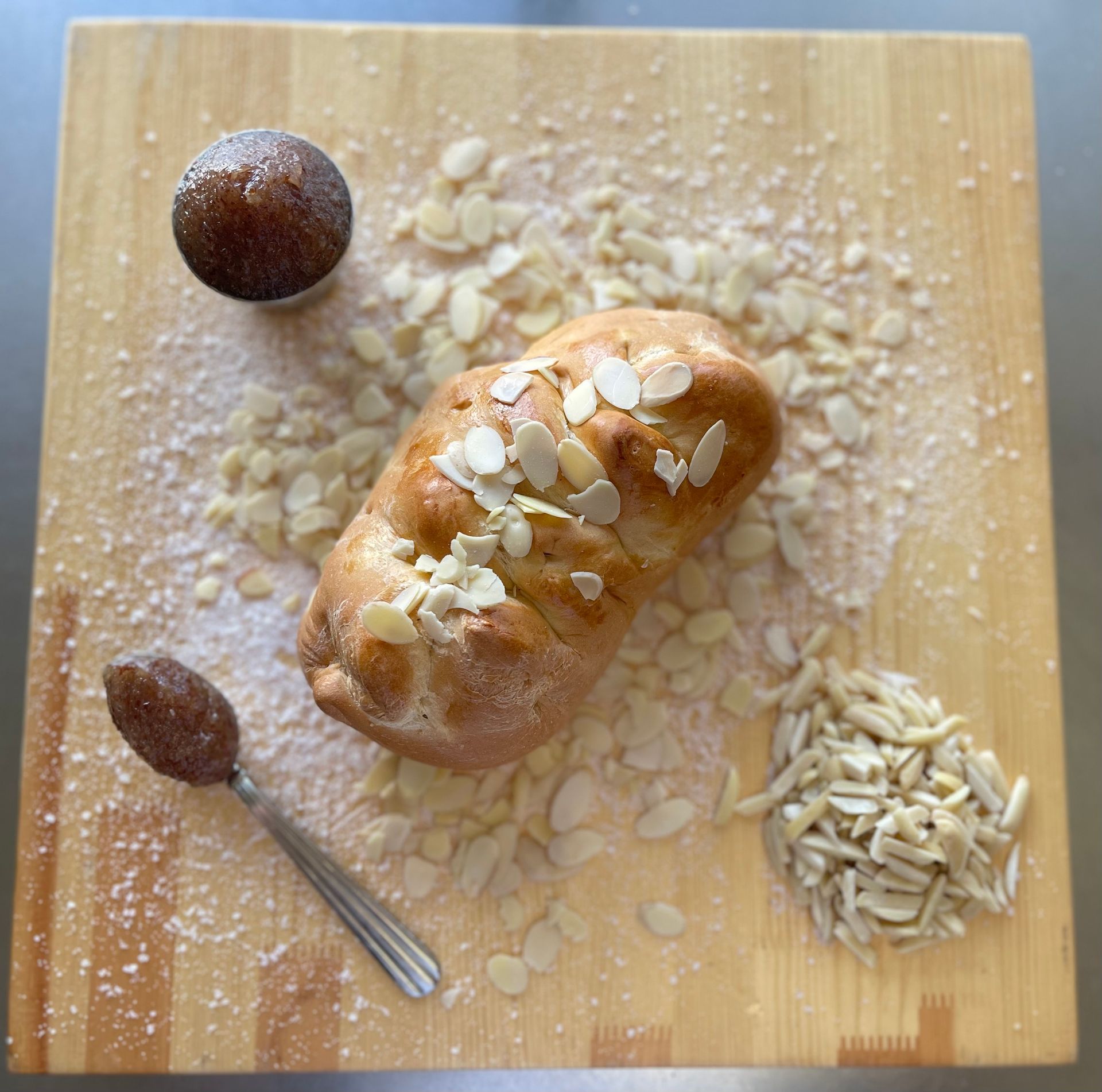 A loaf of bread with almonds on top is on a wooden cutting board.