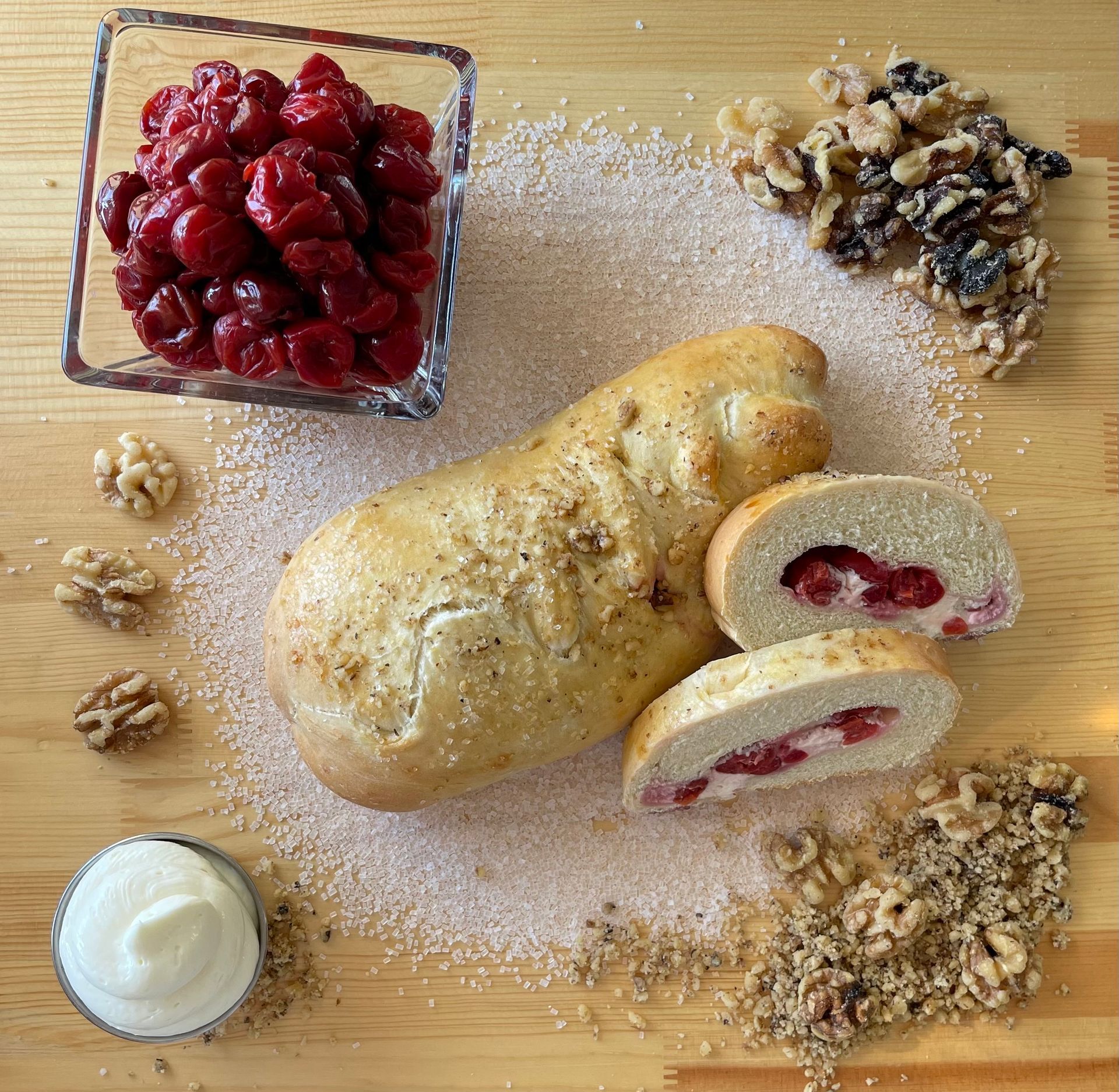 A loaf of bread is sitting on a wooden table next to a bowl of cherries and walnuts.
