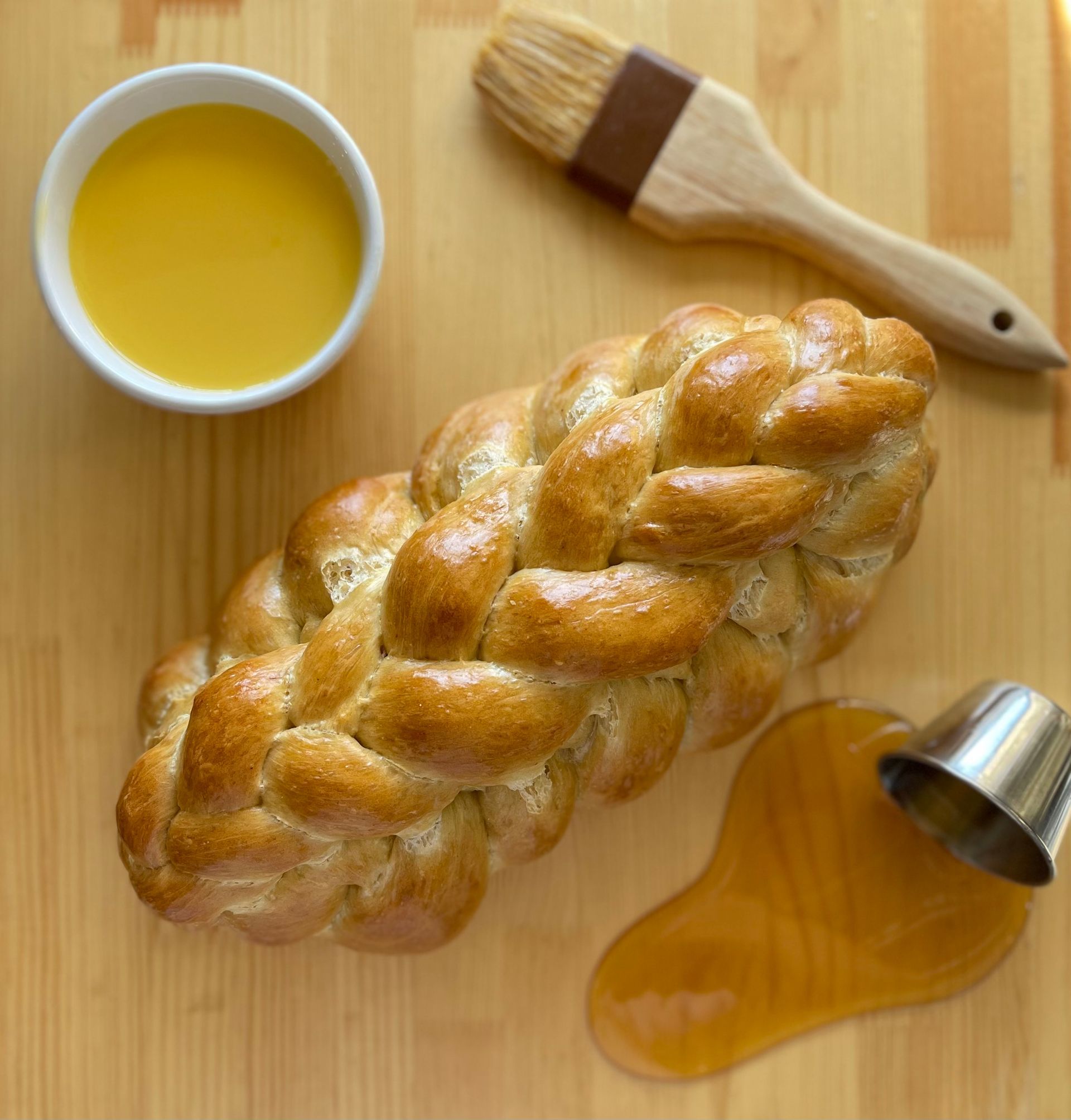 A braided loaf of bread next to a bowl of oil and a brush