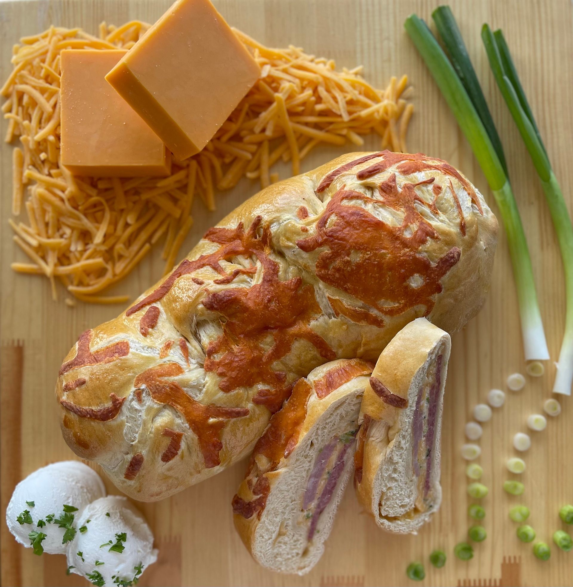 A loaf of bread is surrounded by cheese and green onions