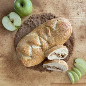 A loaf of bread is sitting on a wooden cutting board next to apples.