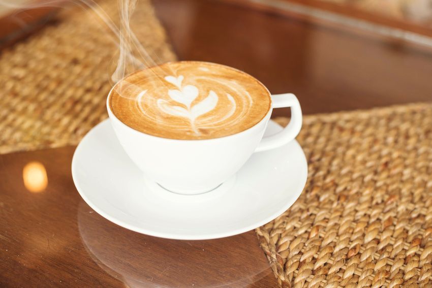 A cup of cappuccino is sitting on a saucer on a table.
