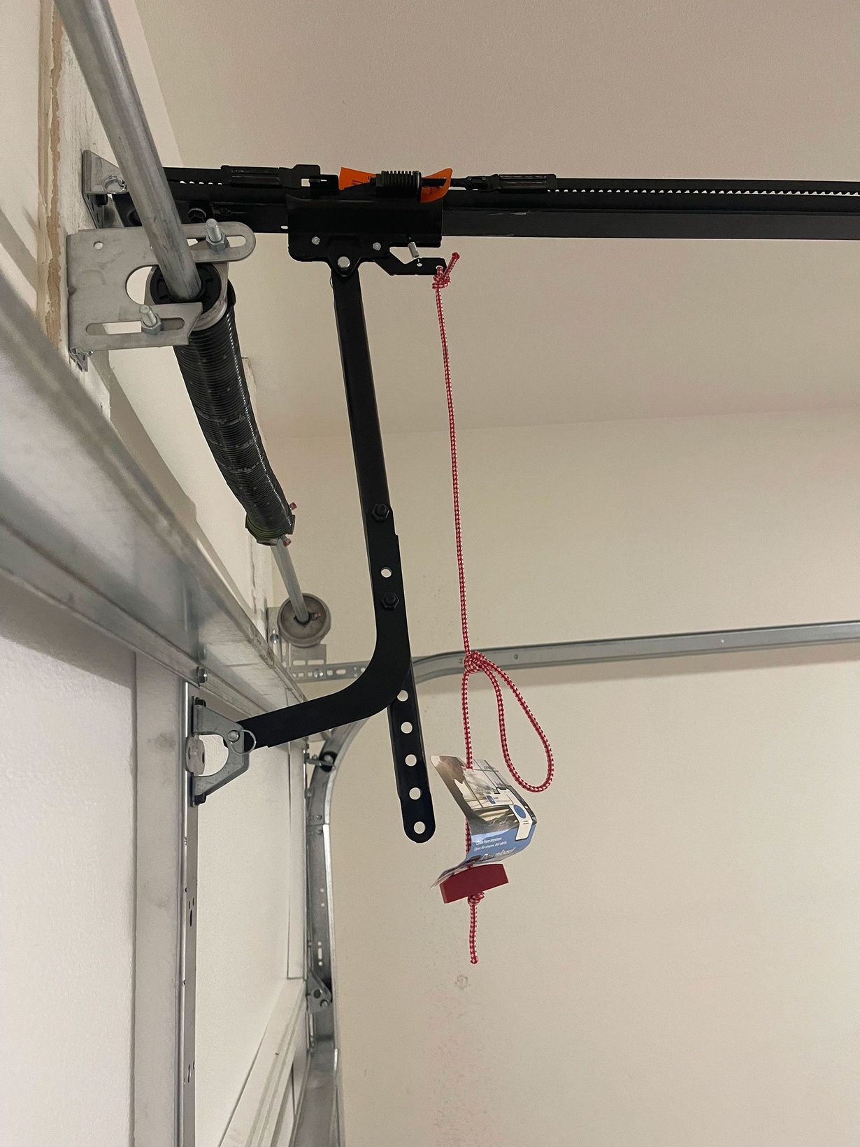 Garage door opener mechanism with a red emergency release cord.