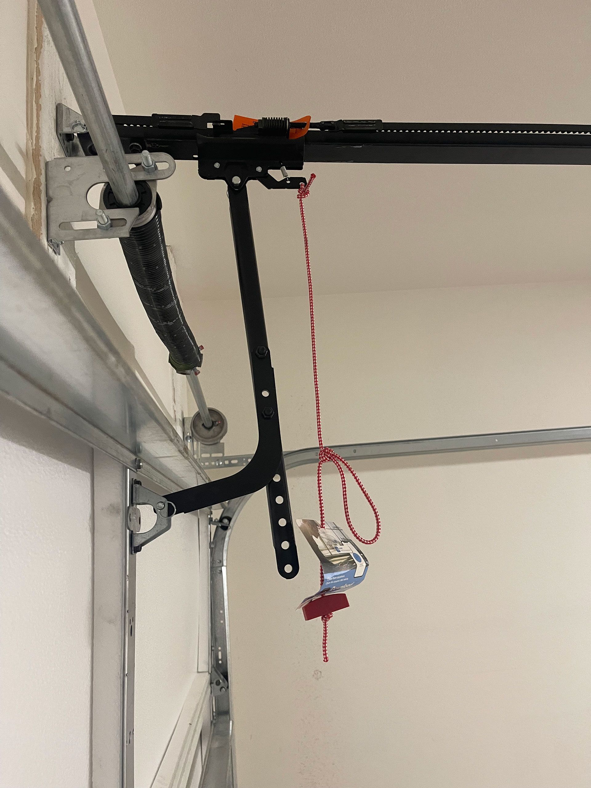 Garage door opener mechanism with a red emergency release cord.