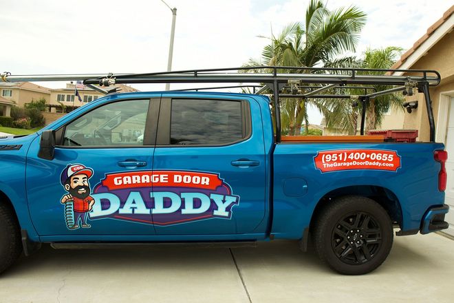 Blue pickup truck with "Garage Door Daddy" logo and rack parked in a residential area.
