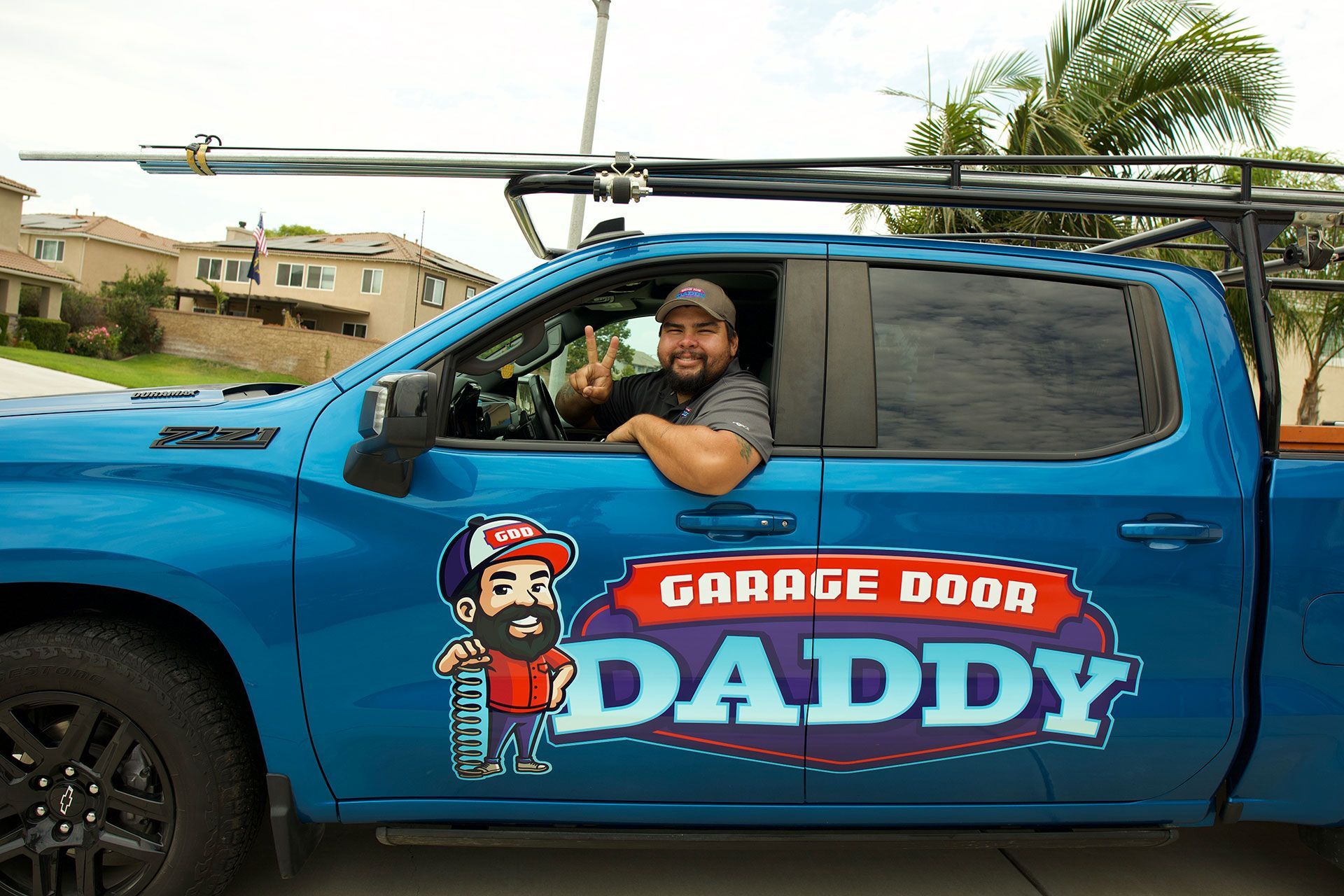 Man in blue truck with "Garage Door Daddy" logo gives peace sign.