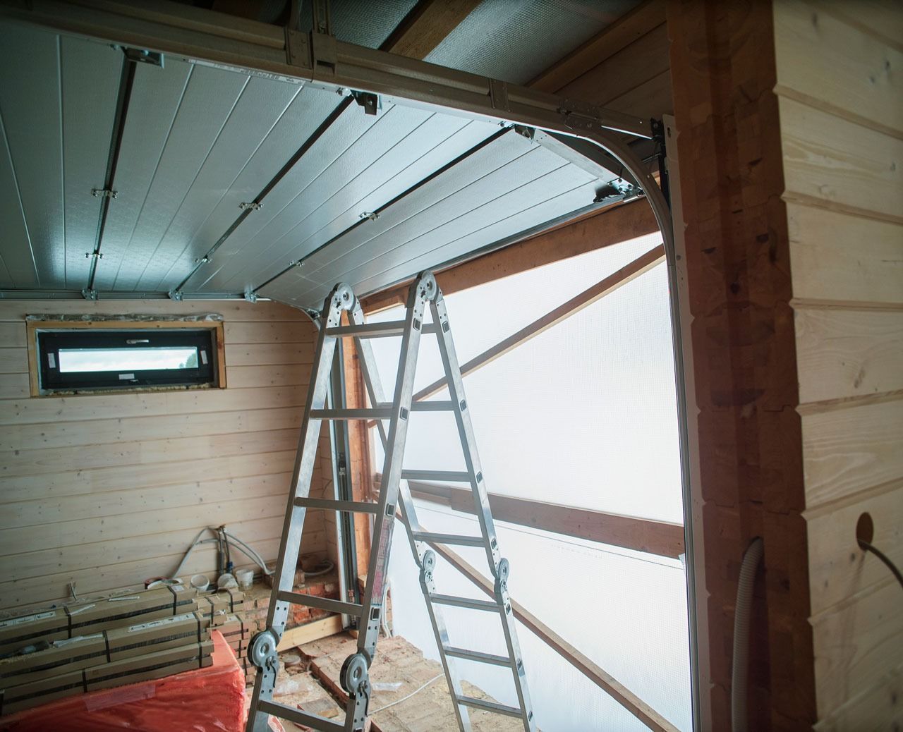 Ladder inside unfinished structure with open doorway and panelled ceiling.