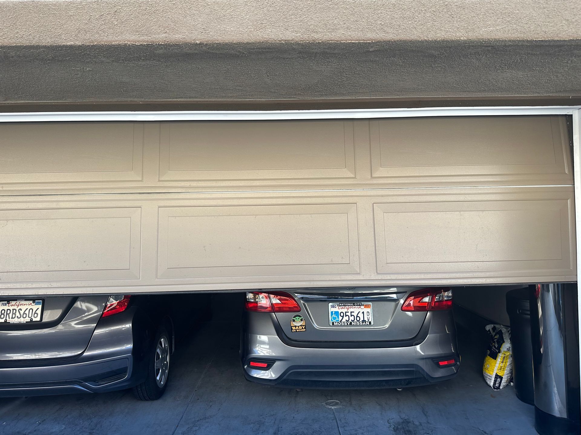 Two cars parked inside a garage, partially obscured by an open tan garage door.