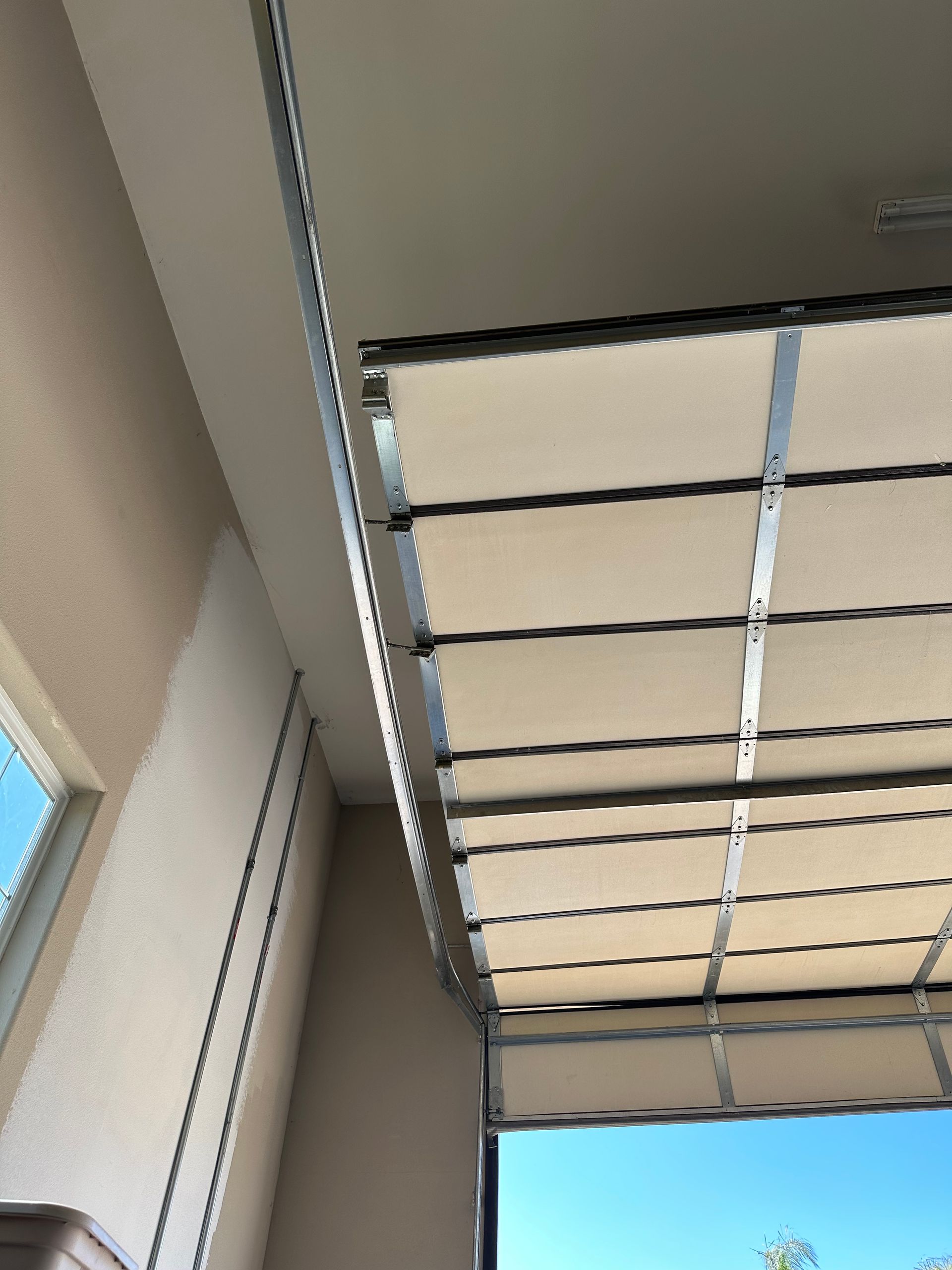 Beige retractable awning partially open, mounted on a porch ceiling with blue sky visible.