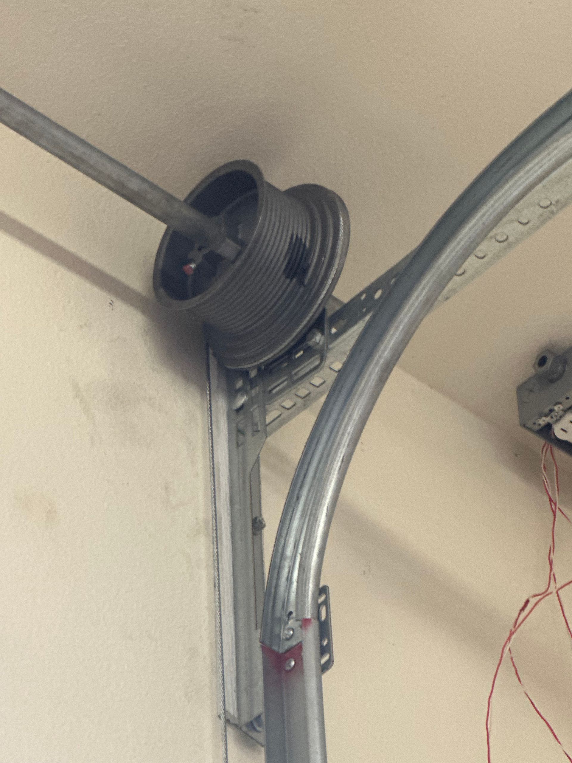 Garage door spring and track assembly. The spring is metal and coils around a spool. A curved track is mounted on the wall.