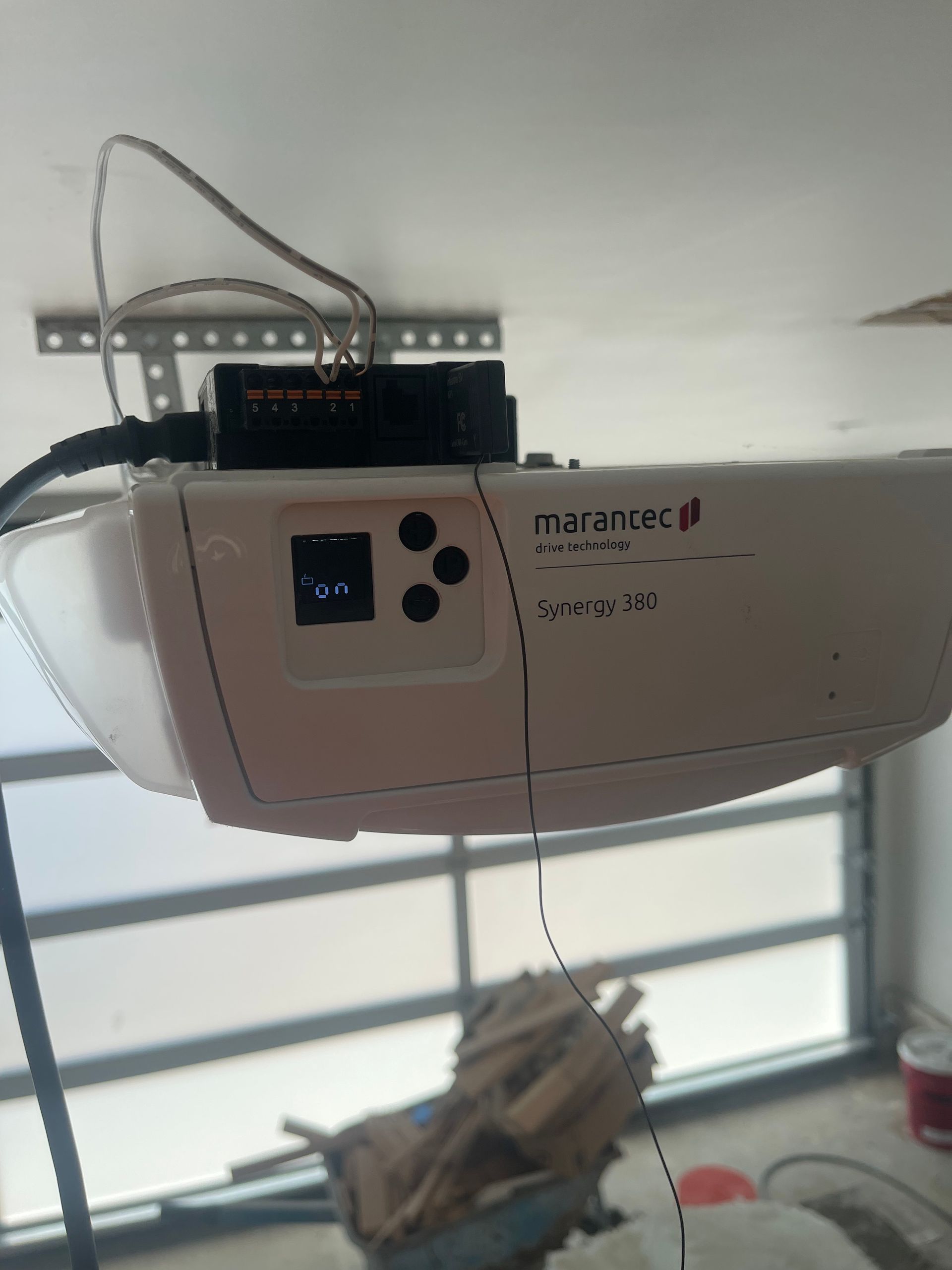 White Marantec garage door opener with control buttons and a connected black device.