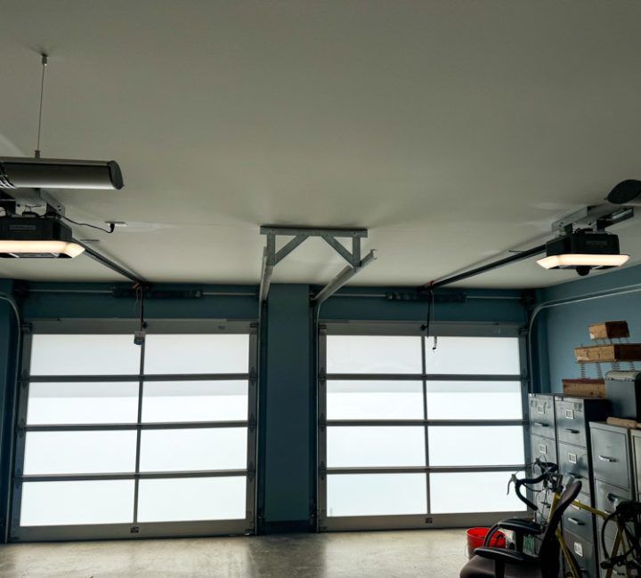 Garage interior with two closed glass doors, garage door openers, and a gray floor.