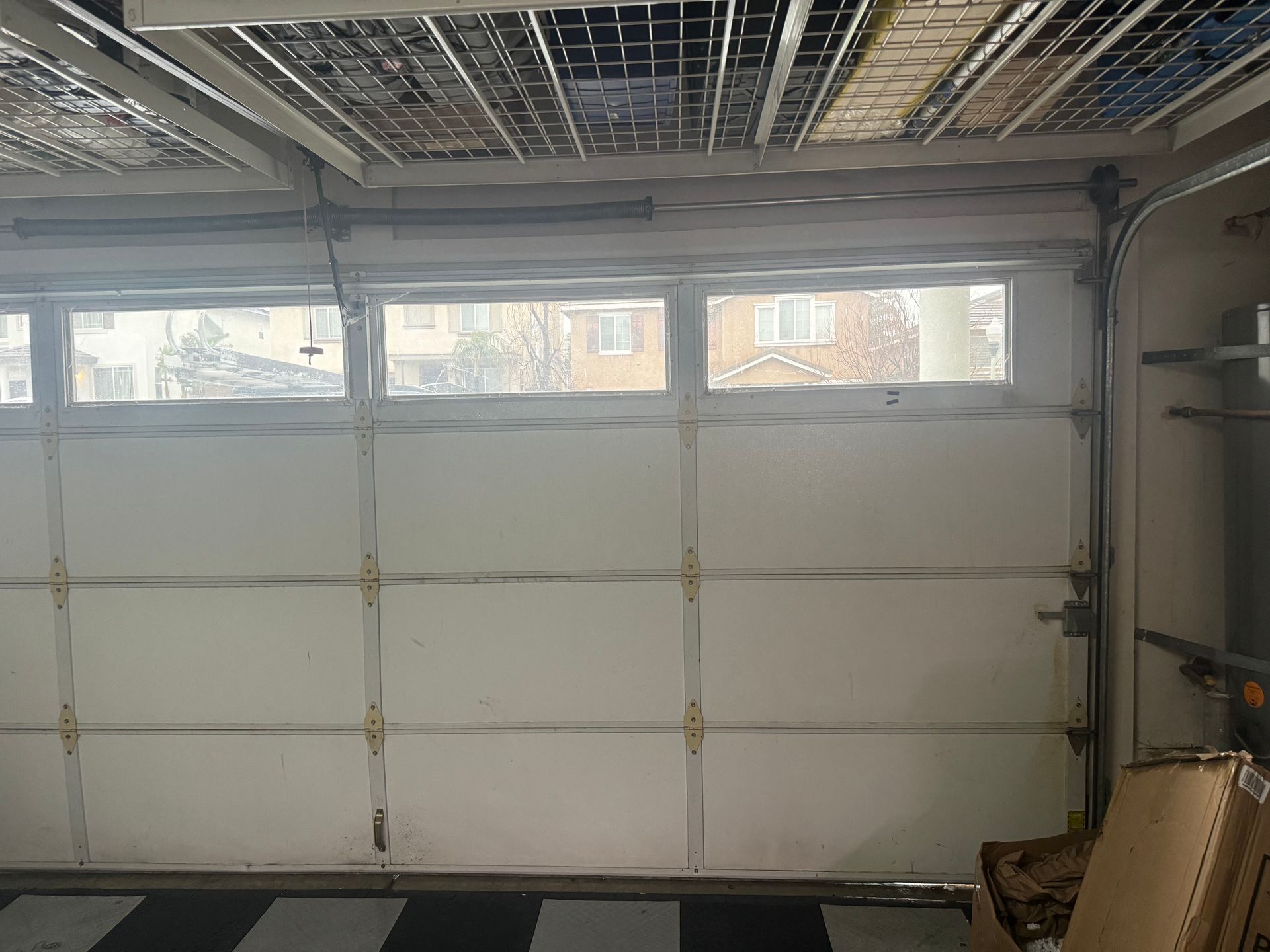 Garage interior with closed white garage door, overhead storage, and windows.
