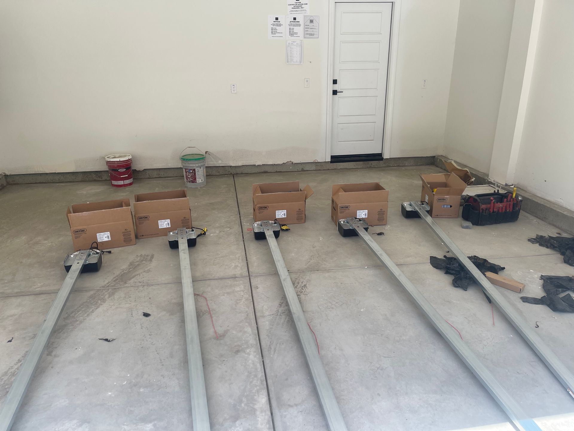 Garage with door, concrete floor, boxes, metal tracks, and paint buckets.