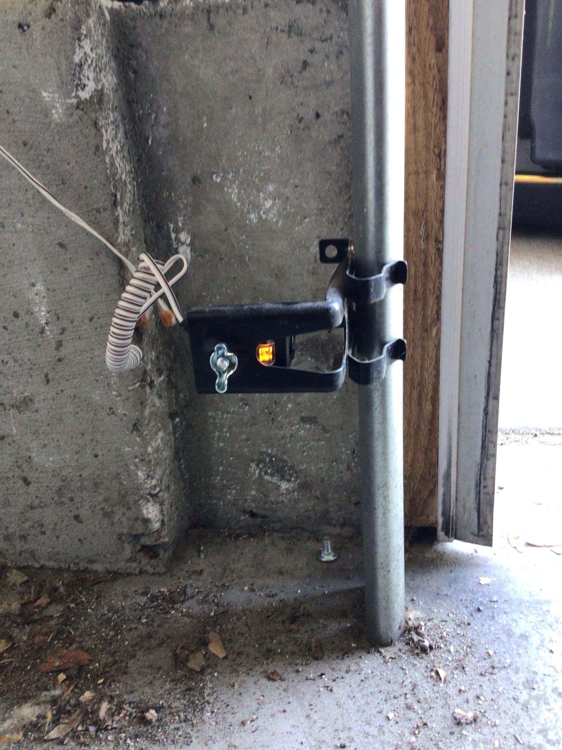 Black garage door sensor mounted on a metal pipe, near a concrete wall.