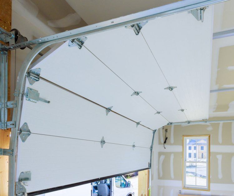 Garage door, white panels, partially open, revealing a view of a house through a small window.