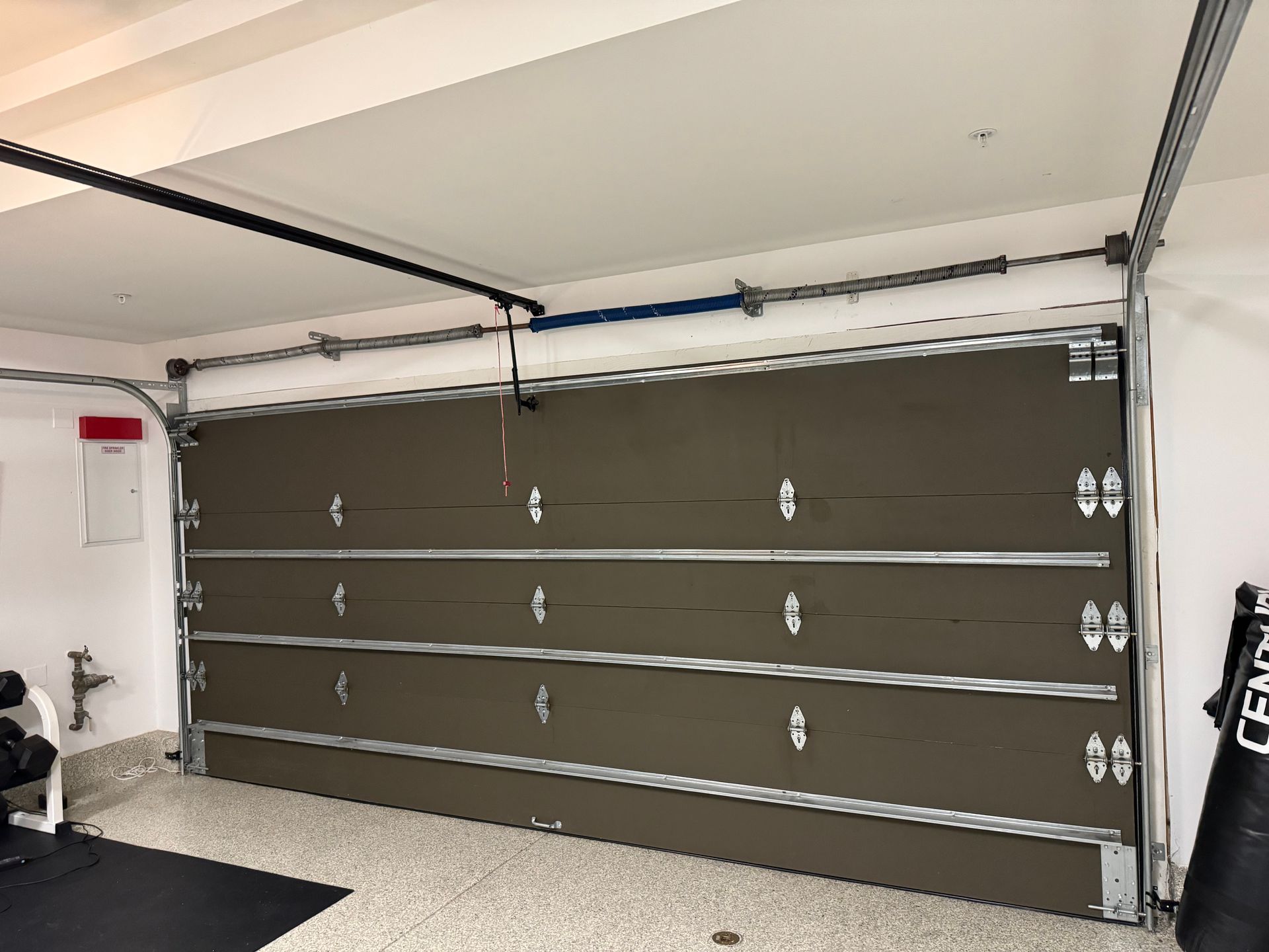 Brown garage door, partially open, inside a garage with equipment visible.