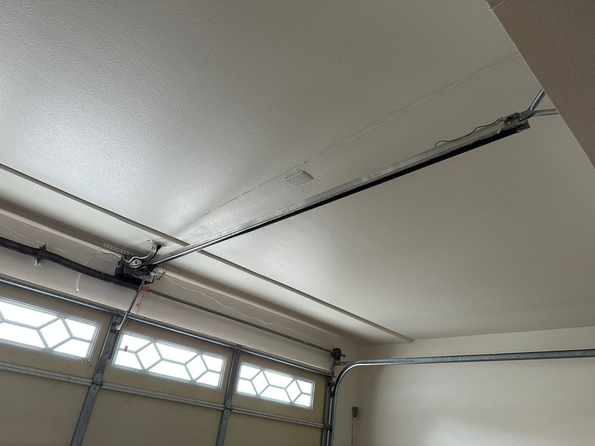 Garage door opener track and connected door mechanism on a white ceiling.
