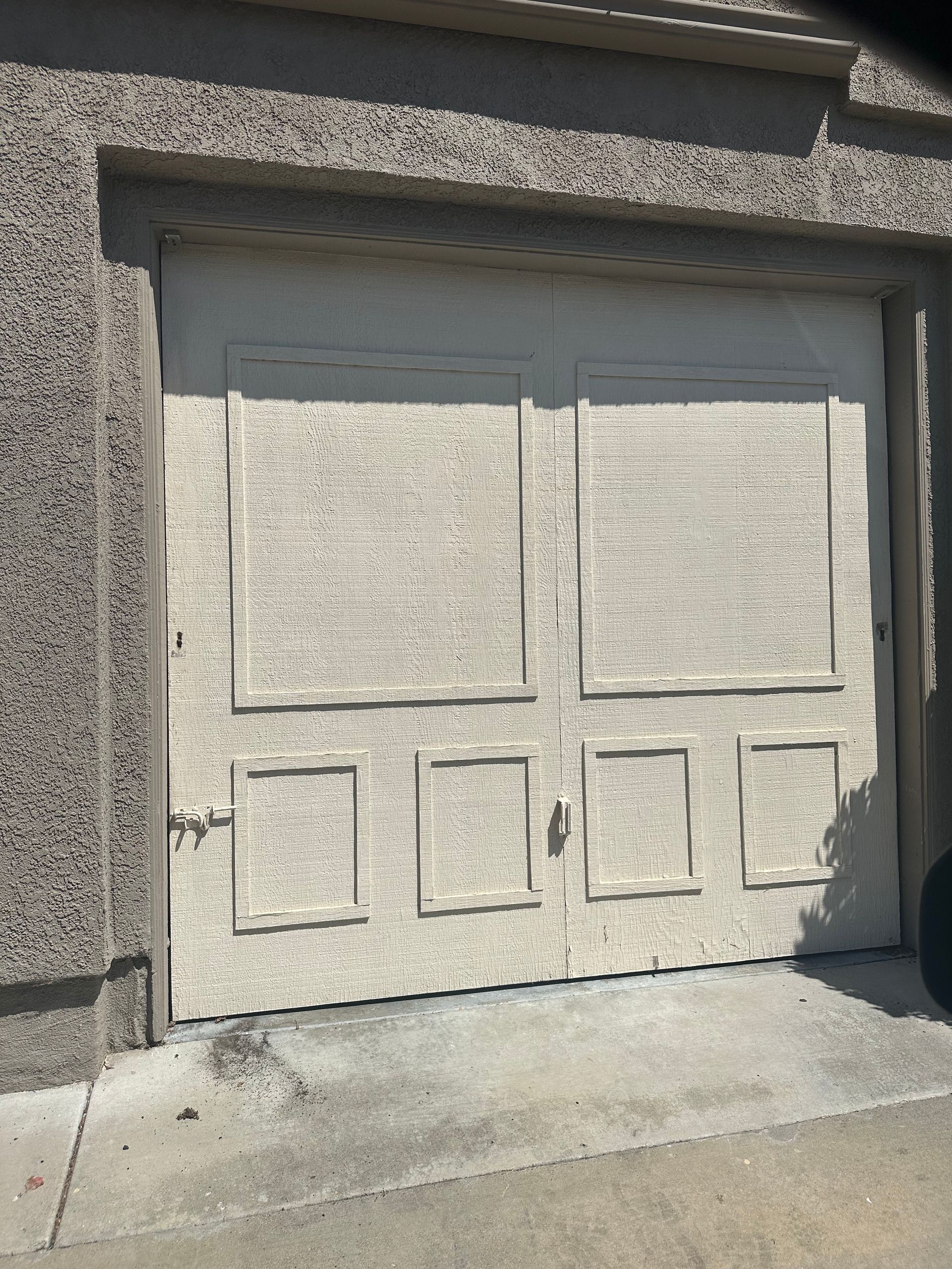 Cream-colored garage door with decorative panels, set in a stucco-textured wall.